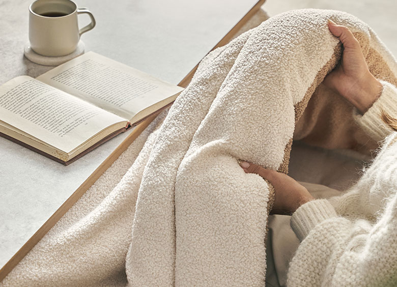 中綿が詰まって保温性の高いこたつ布団と、女性がその中に入ってあたたまっているイメージ